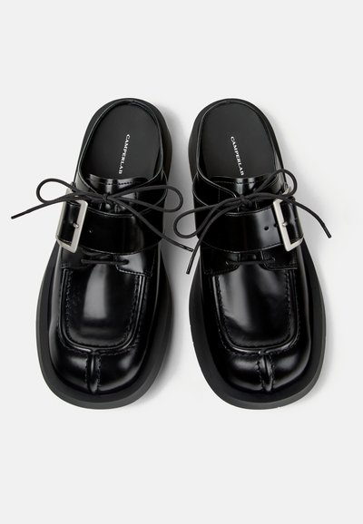 Chaussures en cuir noires à bout carré avec semelles épaisses, lacets et détails à boucle, vues de dessus sur fond blanc.