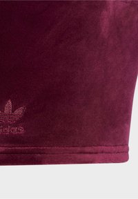 Burgundy sammetstopp med en slät textur. Har en broderad vit logotyp i botten och rena sömmar längs fållen.