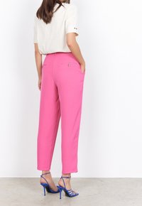 Pantalons taille haute roses avec une coupe droite, dotés de deux poches arrière et de détails en bouton, associés à des escarpins bleus à lanières.