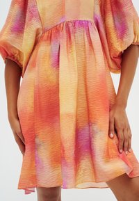 Abito colorato caratterizzato da un tessuto testurizzato in tonalità di arancione, rosa e viola, con maniche a sbuffo e dettaglio in vita arricciato.