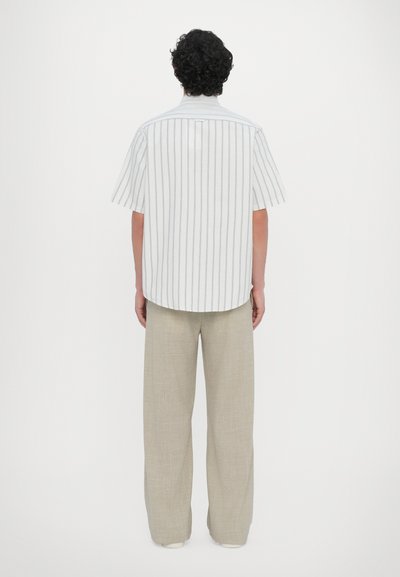 Kortermet stripete skjorte i lett stoff med vertikale grå striper, kombinert med beige, vide bukser og hvite slip-on sko.