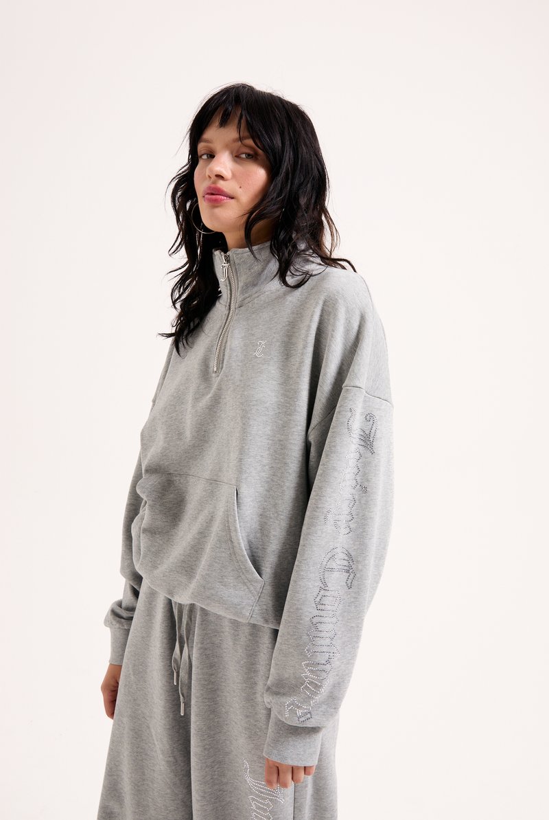 Γκρι κοντό φούτερ με μισό φερμουάρ, μπροστινή τσέπη και γυαλιστερά γράμματα κατά μήκος του μανικιού. Φτιαγμένο από μαλακό ύφασμα με άνετη εφαρμογή.