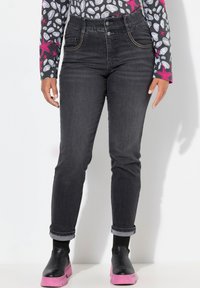 Jeans de mezclilla negros de tiro alto con detalles de costura sutil y diseño clásico de 5 bolsillos. Combinados con botas de plataforma negras y rosas.