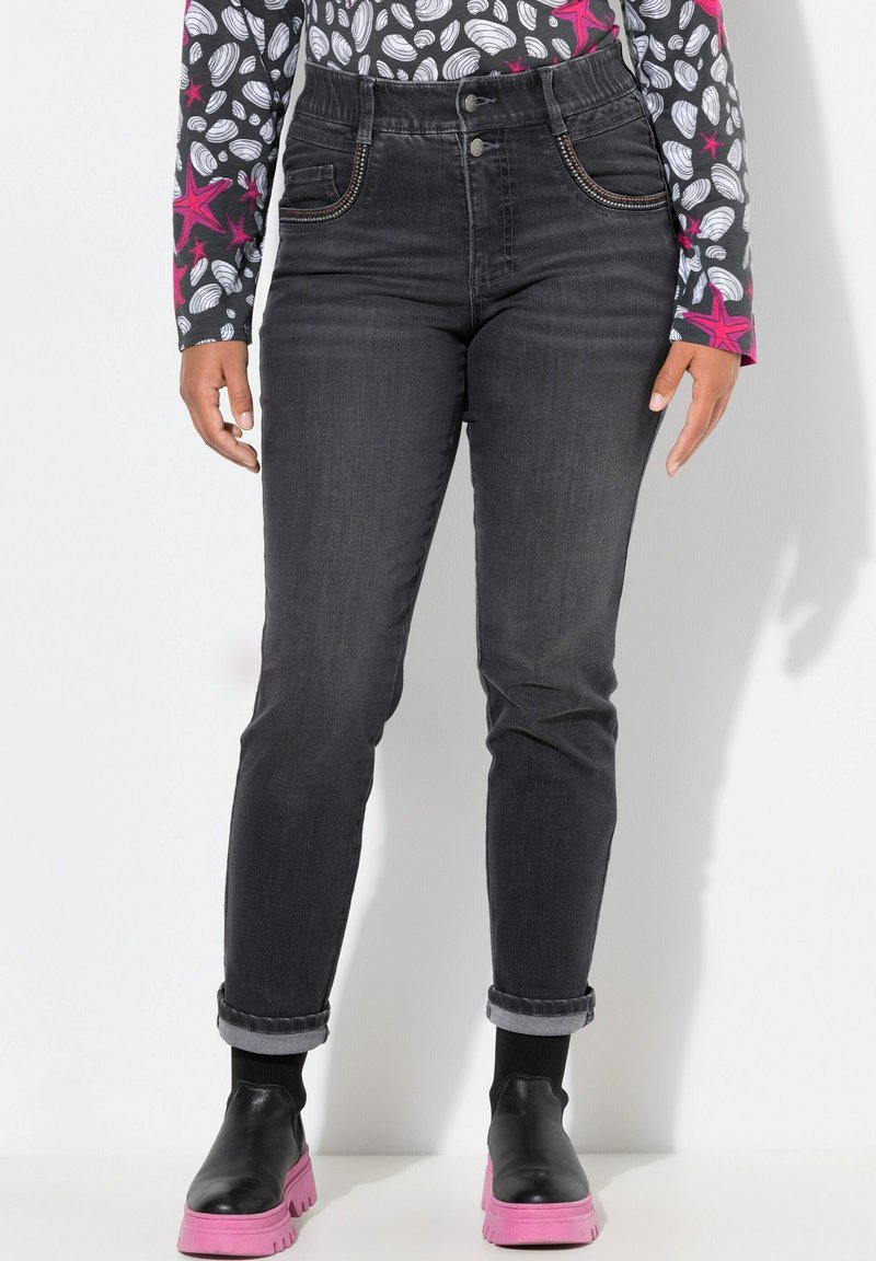 Jeans de mezclilla negros de tiro alto con detalles de costura sutil y diseño clásico de 5 bolsillos. Combinados con botas de plataforma negras y rosas.