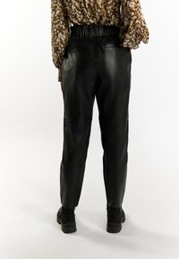 Pantaloni in pelle nera con vita elastica e due tasche posteriori, caratterizzati da una superficie liscia e una forma affusolata, abbinati a stivali neri.