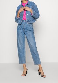 Krótkia dżinsowa kurtka i jasnoniebieskie jeansy z wysokim stanem, zestawione z jaskraworóżową bluzką, dopełnione czarnymi sandałami na słupku.