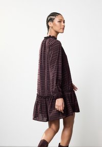 Voolava marooni värvi kleit pikkade varrukatega, volditud kaelusega ning kihilise alläärega. Omab peent triibulist mustrit ning taljes kogutud detaile.