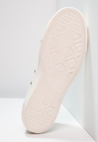 Semelle de basket blanche avec une bande de caoutchouc texturée, présentant un motif géométrique et un détail de logo, des bords lisses et aucun élément matériel visible.