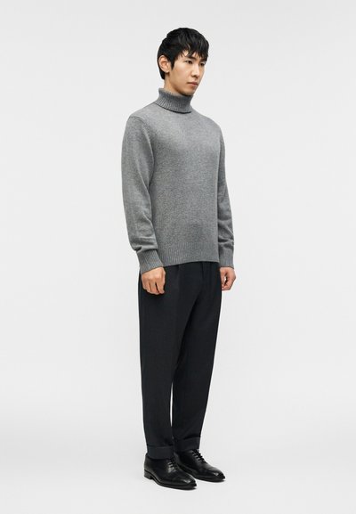 Γκρι πλεκτό πουλόβερ με ψηλή λαιμόκοψη, συνδυασμένο με μαύρο παντελόνι με λεπτές ρίγες και μαύρα παπούτσια. Απλός, μοντέρνος σχεδιασμός με άνετη εφαρμογή.