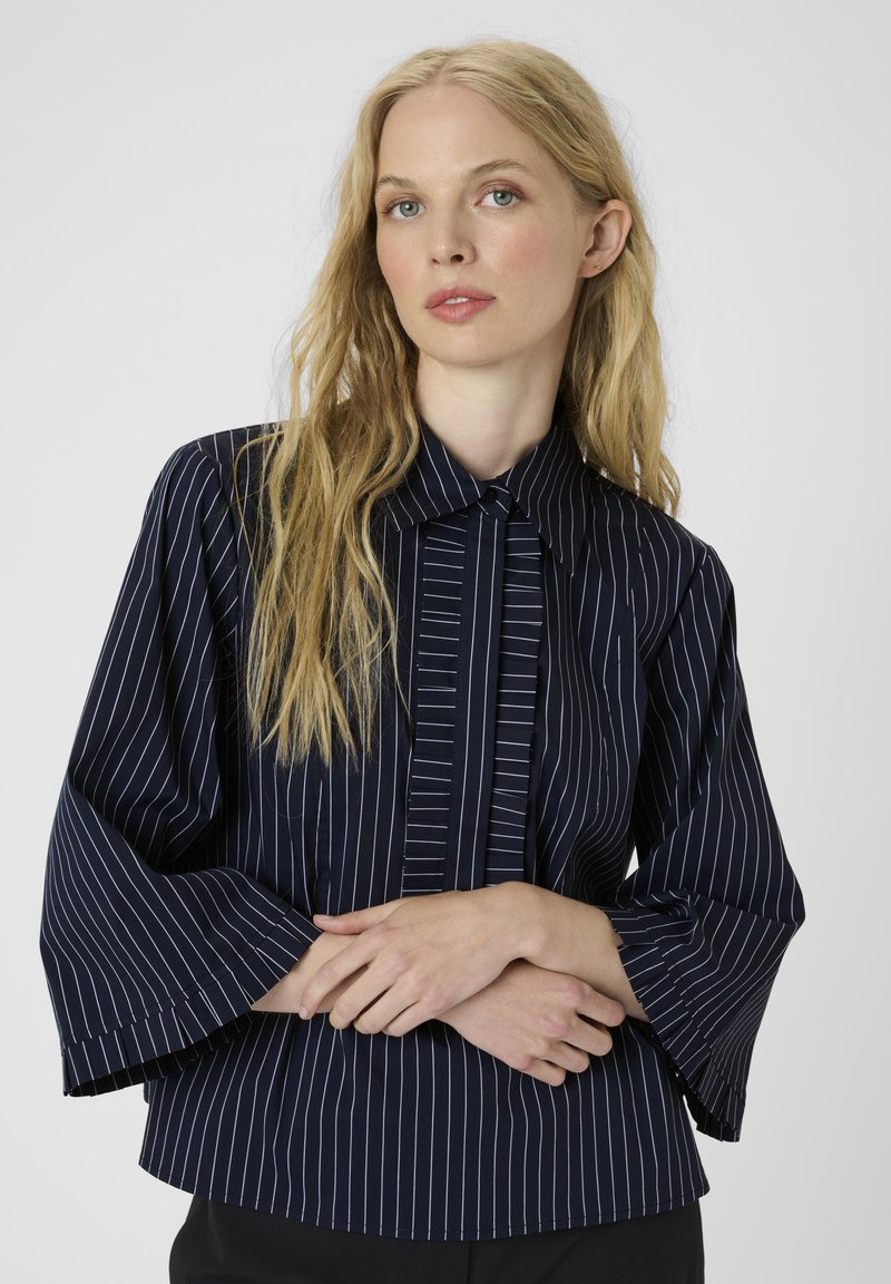 Marineblauw gestreept shirt met een kraag, geplooide voorkant en uitlopende mouwen. Het materiaal lijkt glad te zijn met contrasterende witte strepen.