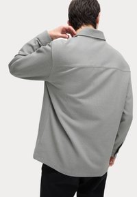 Suéter gris con un cuello estructurado y mangas largas. Tejido texturizado con un ajuste relajado, que presenta un dobladillo recto y detalles discretos.