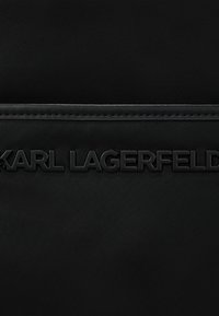 Bolsa de tela negra con una textura suave y el logo en relieve "KARL LAGERFELD" en color a juego, acentuado por un detalle de costura en la parte superior.