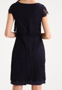 Robe en dentelle bleu marine avec des manches courtes, motif floral raffiné, ourlet en forme de bord scallopé et une fermeture éclair invisible au dos. Intérieur doublé pour plus de confort.