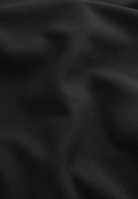 Tissu noir à la texture lisse, présentant un léger éclat et une subtile élasticité. La surface montre des plis et des creux doux.