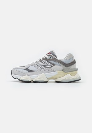Lav top grå og hvid atletisk sneaker med mesh- og ruskindspaneler, hvide snørebånd og en tyk, tekstureret sål.