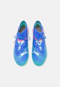 Zapatillas deportivas de textura azul con una suela verde degradada, detalles en rosa y cordones azules. Cuentan con una parte superior de malla con detalles de logo.