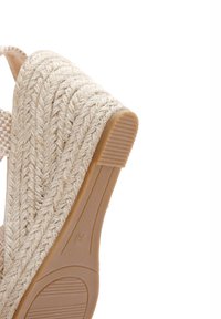 Sandaletta con zeppa beige con una texture in corda intrecciata sul tallone, suola in gomma e una finitura liscia. Presenta una cinturino a scacchi per un tocco di dettaglio.