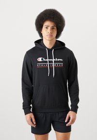 Svart hettegenser laget av bomull, med en hvit snøring, frontlomme, og rød tekst som sier "Champion ATHLETICWEAR" på brystet.