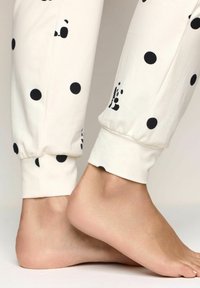 Pantaloni da pigiama bianchi con pois neri, con una fascetta elastica alla caviglia. Materiale in cotone morbido con una texture liscia.