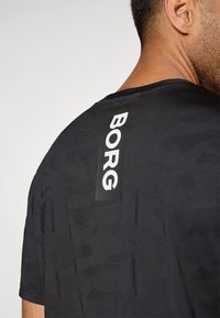 Μαύρο αθλητικό μπλουζάκι με υφή, που διαθέτει μαύρη ετικέτα με λευκά γράμματα που γράφουν "BORG" στον πίσω λαιμό.