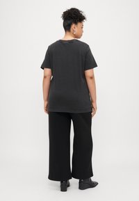 Tricou negru din bumbac, cu mâneci scurte și o croială lejeră, purtat cu pantaloni largi negri. Textură netedă, design simplu, fără modele.