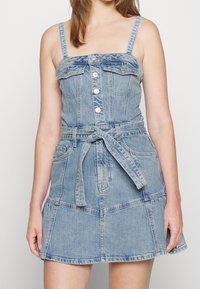 Sukienka dżinsowa w jasnoniebieskim odcieniu, dopasowane body, regulowane ramiączka, zapięcie na guziki z przodu oraz pasek w talii, z kloszowaną spódnicą.