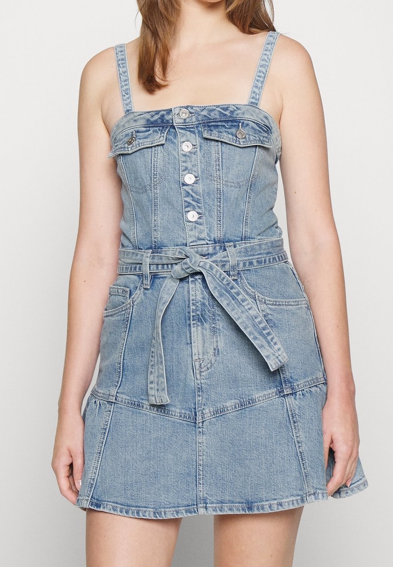 Sukienka dżinsowa w jasnoniebieskim odcieniu, dopasowane body, regulowane ramiączka, zapięcie na guziki z przodu oraz pasek w talii, z kloszowaną spódnicą.