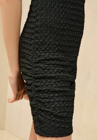 Abito nero aderente con tessuto testurizzato e gathered caratterizzato da un motivo a zigzag, che mette in risalto Plissettature intricate lungo il lato.
