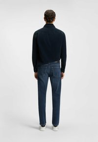 Donkerblauwe corduroy overhemd met een gestructureerde kraag, gecombineerd met donkerblauwe denimspijkerbroek en witte sneakers, gezien vanaf de achterkant.