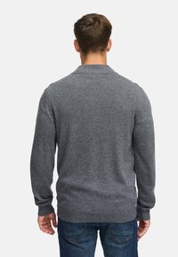 Grå stickad tröja med ribbad krage och mudd, med en avslappnad passform och en texturerad yta. Bakifrån visar den en minimalistisk design.