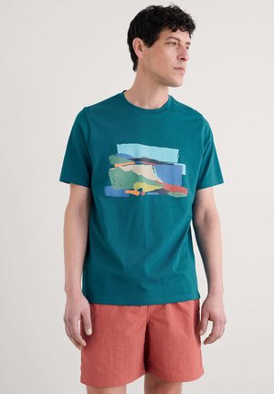 T-shirt en coton teal avec un design graphique abstrait multicolore sur le devant. Associé à des shorts corail, mettant en valeur une coupe décontractée.