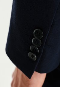 Mankiet granatowego marynarki ze strukturalnym materiałem, z czterema czarnymi guzikami zdobionymi kwiatowym wzorem i subtelnym połyskiem.