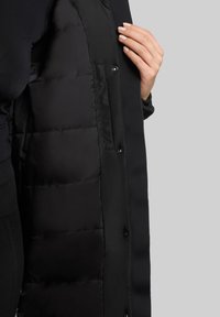 Sort puffer-jakke med en glat overflade og quiltet tekstur indeni, kendetegnet ved trykknapper og et elegant design.
