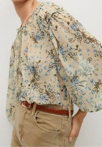 Floral blouse with puff sleeves, featuring a beige background and blue floral pattern. Textured fabric and a tie detail at the neckline.