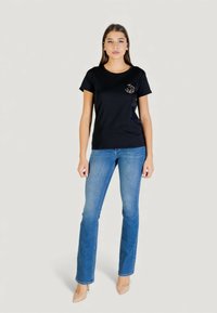 Czarny bawełniany t-shirt z okrągłym dekoltem i krótkimi rękawami, z złotym haftowanym wzorem na piersi, zestawiony z jasnoniebieskimi dżinsami.