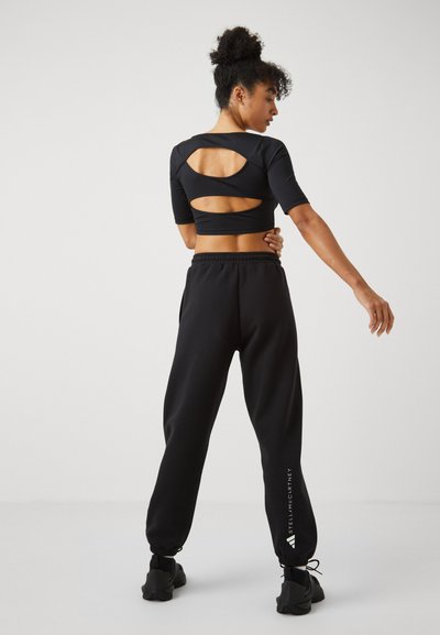 Black athletic top with cut-out back design, short sleeves, paired with black jogger pants featuring elastic waistband and logo detail.
