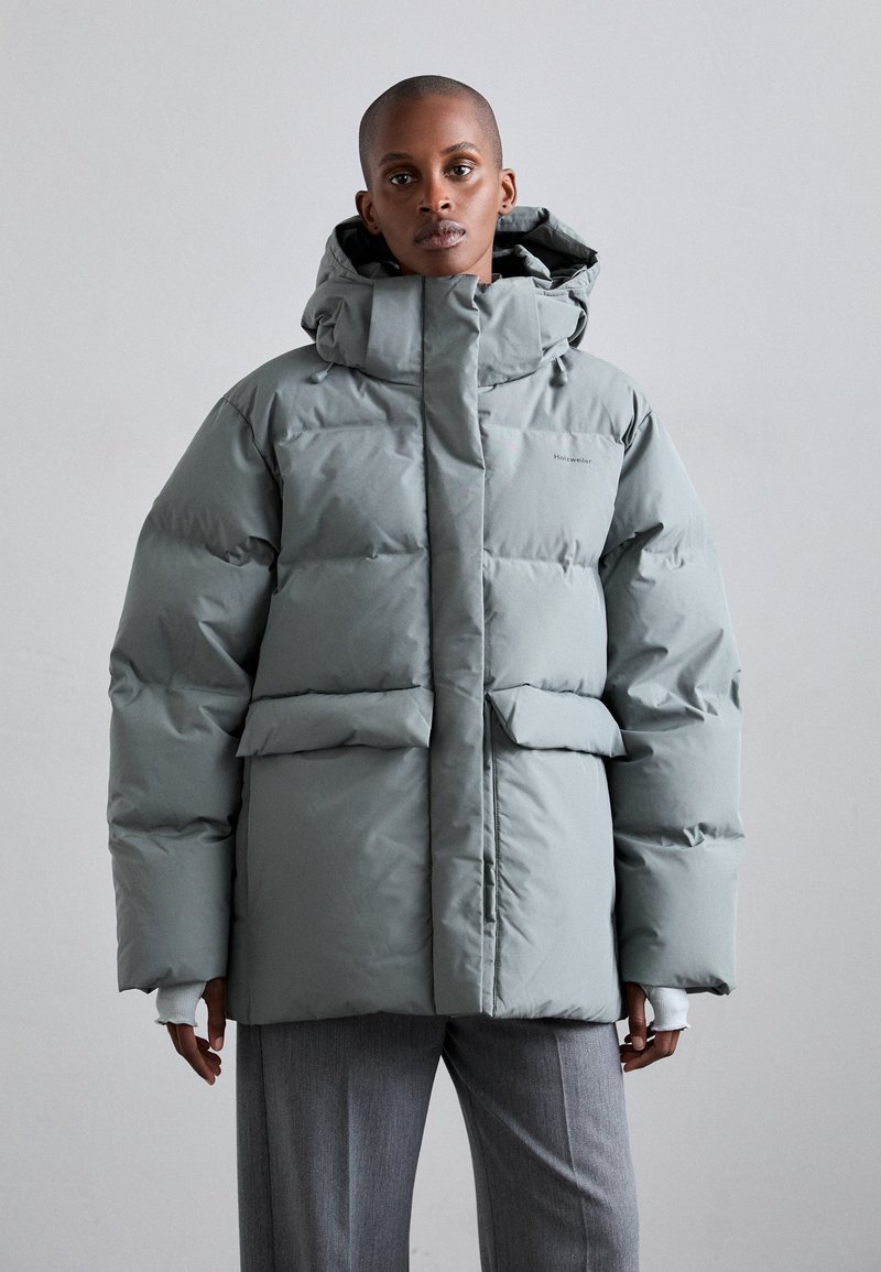 Puffer jacket in light gray with a hood, featuring a boxy shape, two front pockets, and a smooth texture.