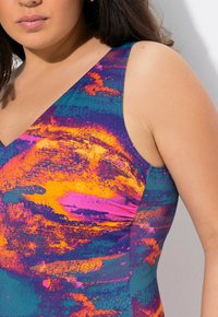 Maillot de bain multicolore avec un décolleté en V, ornée de motifs abstraits vibrants en bleu, orange et rose, fabriqué à partir d'un tissu lisse et extensible.