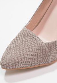 Chaussure plate à bout pointu avec une texture effet peau de serpent grise et une doublure intérieure beige clair sur fond blanc.
