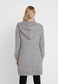 Grå lång stickad cardigan med huva, med ett texturerat mönster, ribbade ärmslut och nederkant, visas bakifrån på en modell.
