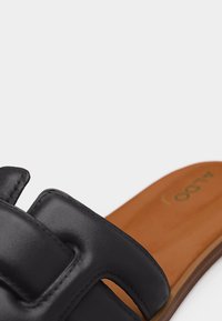 Sandalia negra de cuero sin cierre con correa superior acolchada y plantilla acolchada marrón.