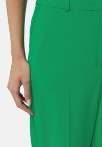 Pantalon vert avec une texture lisse, coupe ajustée et détail de poche latérale. Présente un design droit et de subtils accents de couture.
