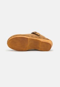 Wildlederschuh mit rundem Zehenbereich, in Tan-Farbe, und dicker Gummisohle. Verfügt über einen seitlichen Riemen mit Schnalle und dekorativen Metallnieten entlang der Kante.