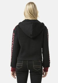 Zwarte cropped hoodie met capuchon, rode accenten op schouders en mouwen, met het woord "ADVENTURER" in het rood gedrukt op de linker mouw.