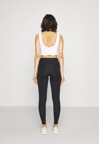 Vit kort topp med rundad baksida, ihopparad med svarta leggings. Leggings har en slät textur, med en tajt passform och detaljer vid anklarna.