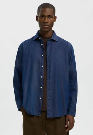 Chemise boutonnée bleu foncé en tissu denim, avec un col classique, des manches longues et une coupe droite avec des boutons blancs.