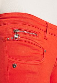 Rode denim jeans met een ritssluiting zak, zilveren hardware en een klein logo accent aan de voorkant. Glad oppervlak met gestikte details.