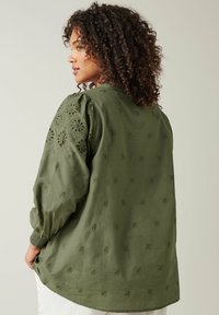 Olivgrüne Bluse mit gestickten floralem Mustern, puffärmeligen Kurzärmeln und lässiger Passform, aus leichtem, strukturiertem Stoff gefertigt.