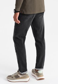 Jeans de denim negro con un corte relajado, que presentan detalles de costura sutiles, combinados con zapatillas beige y gris, y dobladillos remangados.
