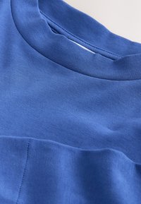 Nahaufnahme eines blauen Sweatshirts mit Rundhalsausschnitt, das die Stoffstruktur und die Nähte in der Nähe des Kragens und des Brustbereichs zeigt.